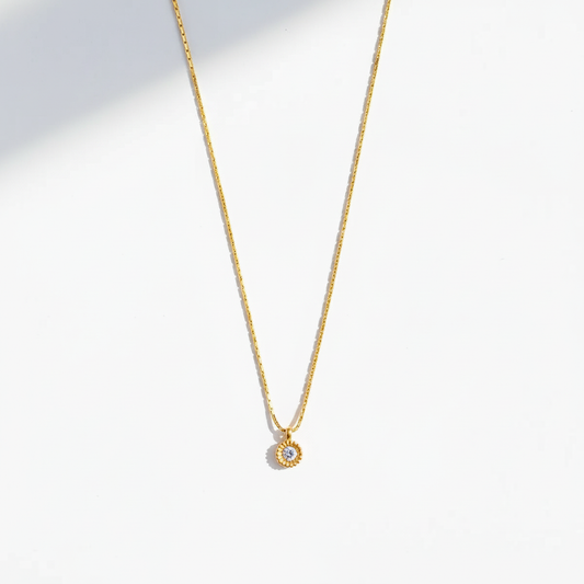 Gold sunflower pendant necklace with straight chain on flat surface