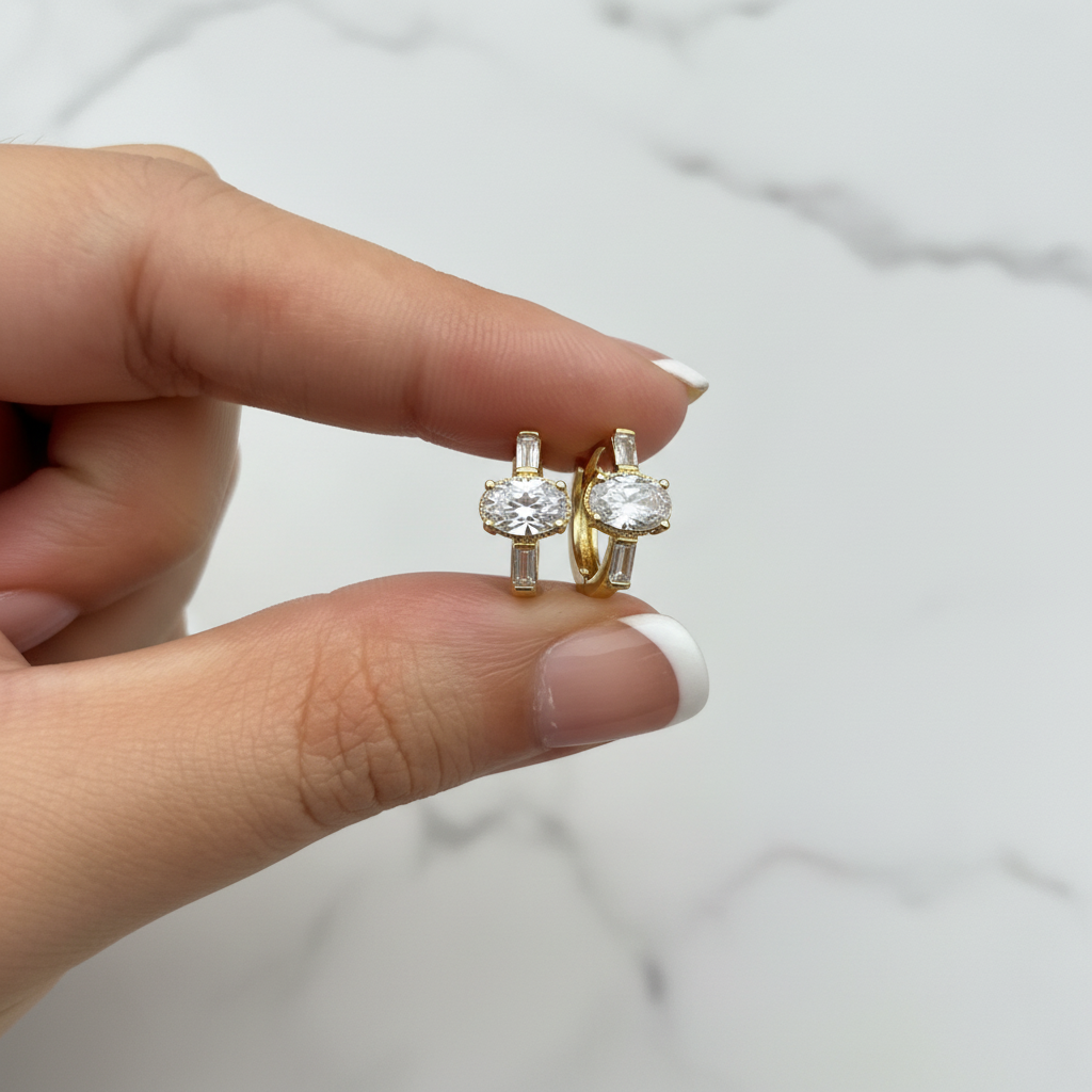 Sterling Huggies triple stone CZ earrings held with French nude nails on white marble