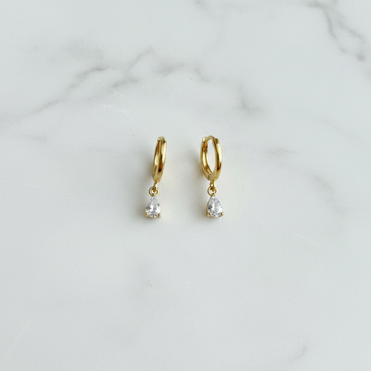 Darcy Huggies gold teardrop CZ huggie earrings on white surface flat lay