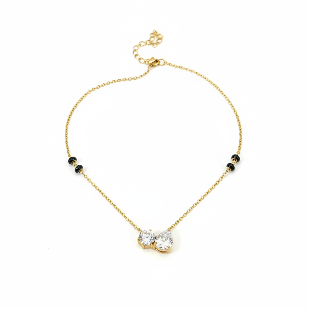 Gold double teardrop pendant necklace with black beads on flat surface