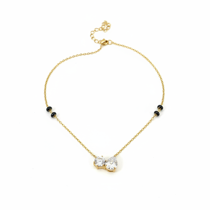 Gold double teardrop pendant necklace with black beads on flat surface