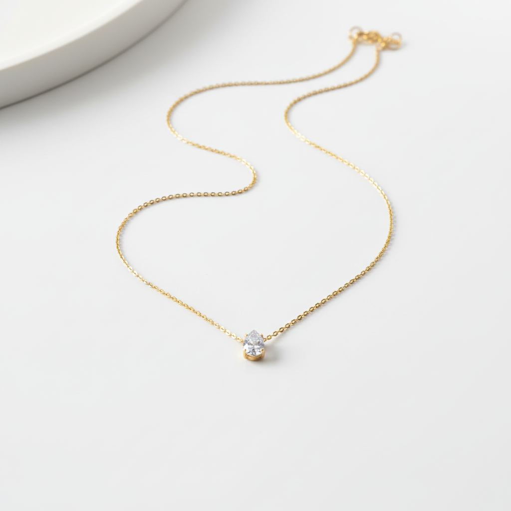 Gold teardrop pendant necklace on flat surface
