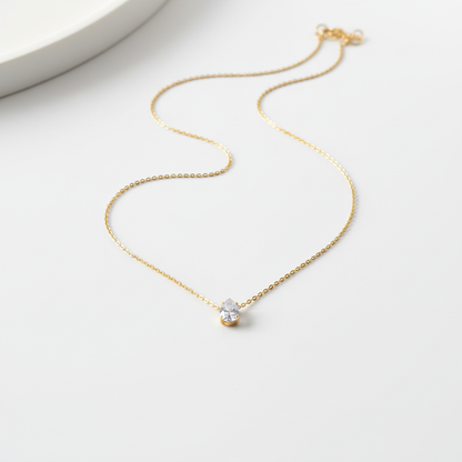 Gold teardrop pendant necklace on flat surface