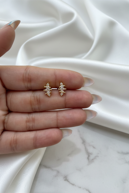 Hand holding gold crystal marquise cross stud earrings on white satin marble background