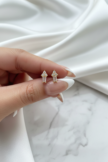 Hand holding gold crystal floral cluster baguette drop stud earrings on white satin marble background
