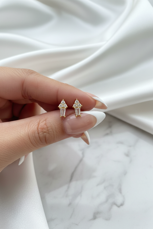 Hand holding gold crystal floral cluster baguette drop stud earrings on white satin marble background
