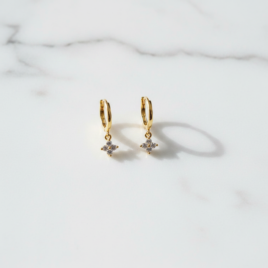 Gold Blush Huggies CZ charm earrings on white surface flat lay