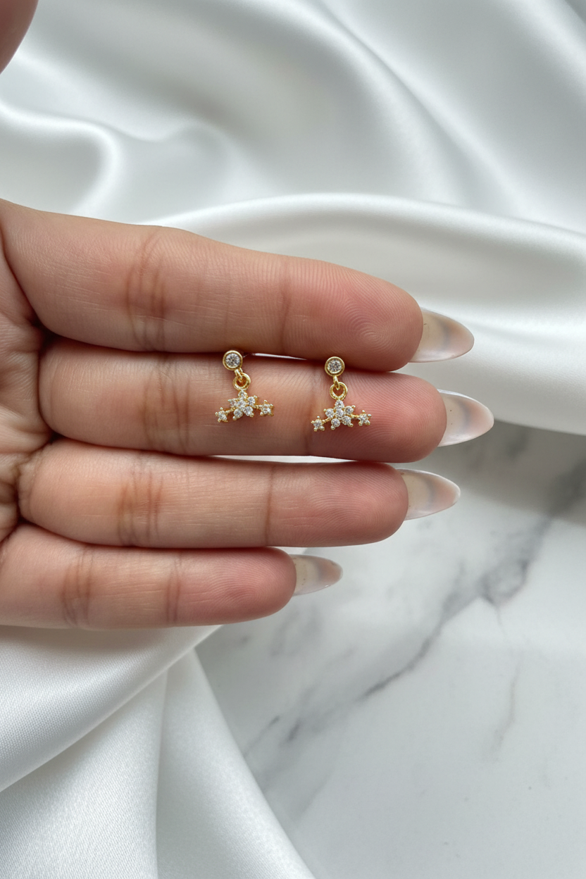 Hand holding gold crystal star constellation drop stud earrings on white satin marble background