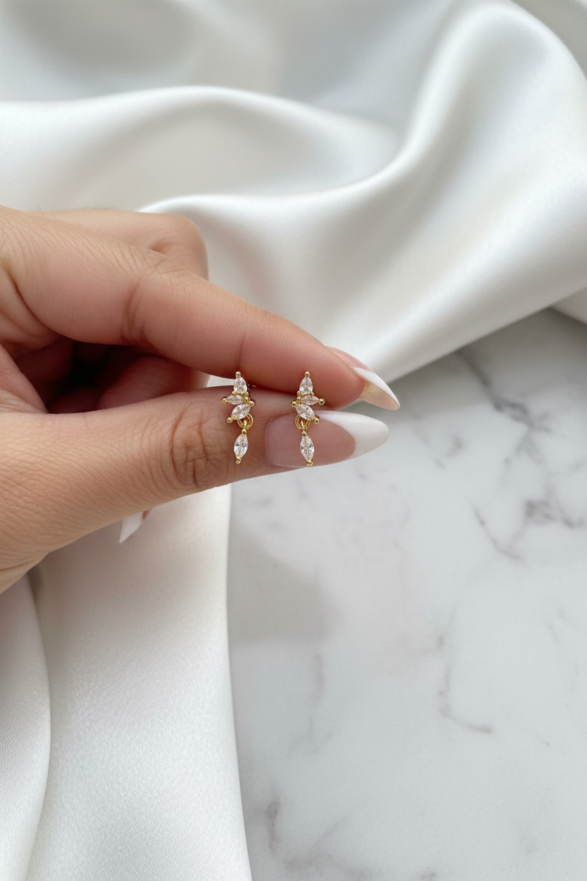 Hand holding gold crystal butterfly floral drop stud earrings on white satin marble background