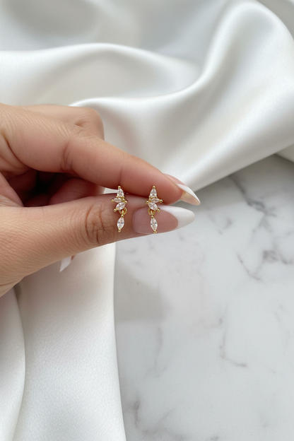 Hand holding gold crystal butterfly floral drop stud earrings on white satin marble background