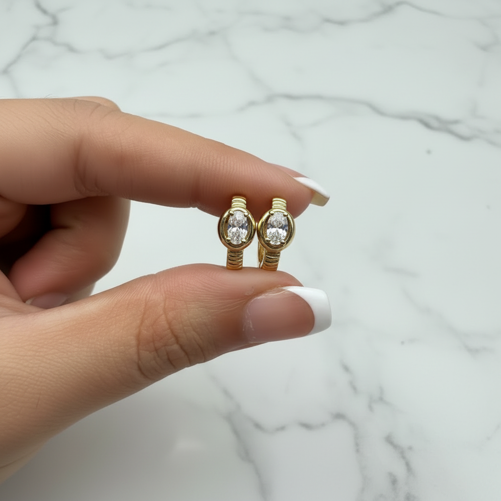 Victoria Huggie oval CZ earrings held with French nude nails on white marble