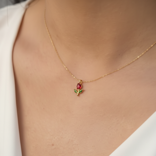 Close-up of red crystal rose bud pendant with green enamel leaves on gold chain on fair skin