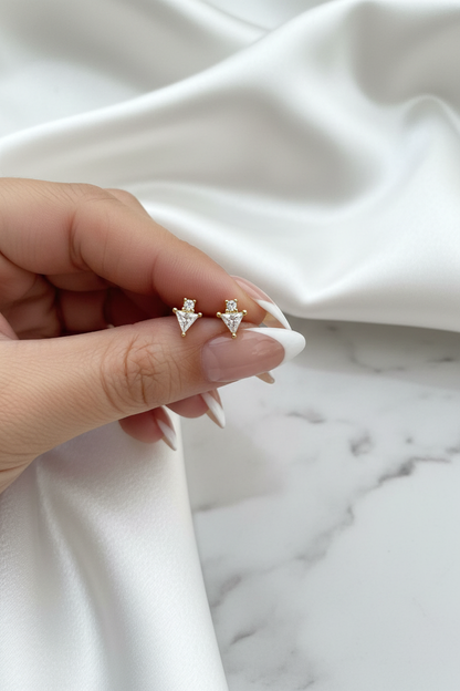 Hand holding gold crystal triangle arrow stud earrings on white satin marble background