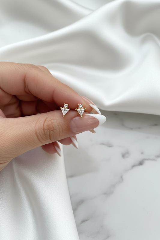 Hand holding gold crystal triangle arrow stud earrings on white satin marble background