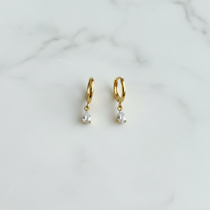 Darcy Huggies gold teardrop CZ huggie earrings on white surface flat lay