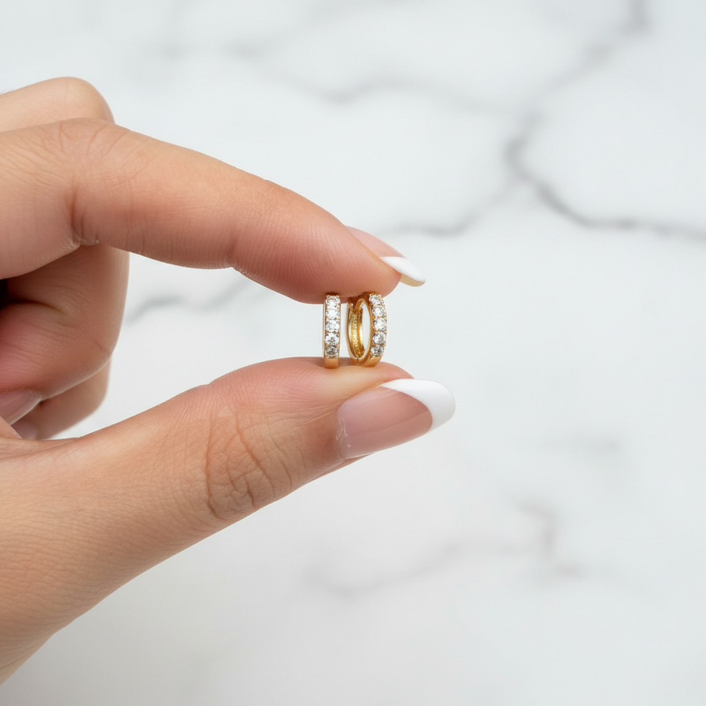 Tara Huggie pavé CZ earrings held with French nude nails on white marble