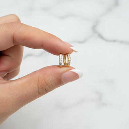Tara Huggie pavé CZ earrings held with French nude nails on white marble