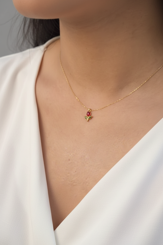 Fair-skinned model wearing gold red rose bud pendant necklace at collarbone on soft neutral background